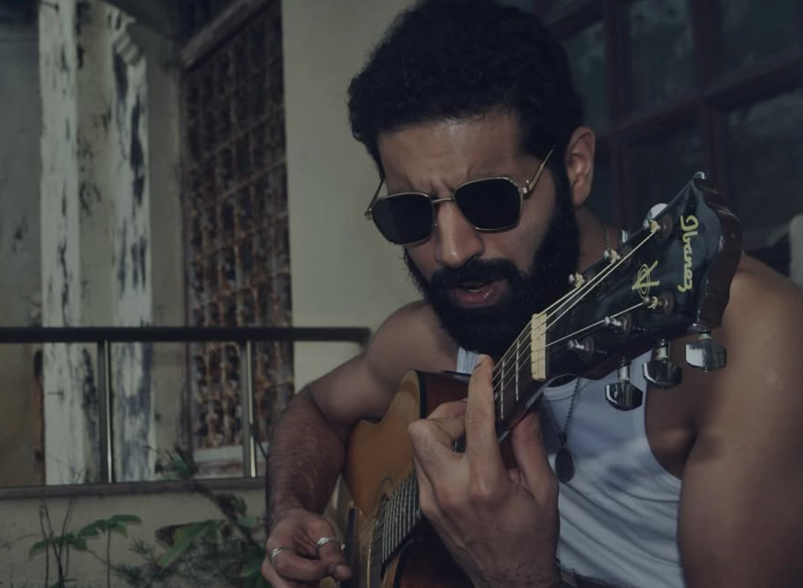 Azamaan playing acoustic guitar on a balcony
